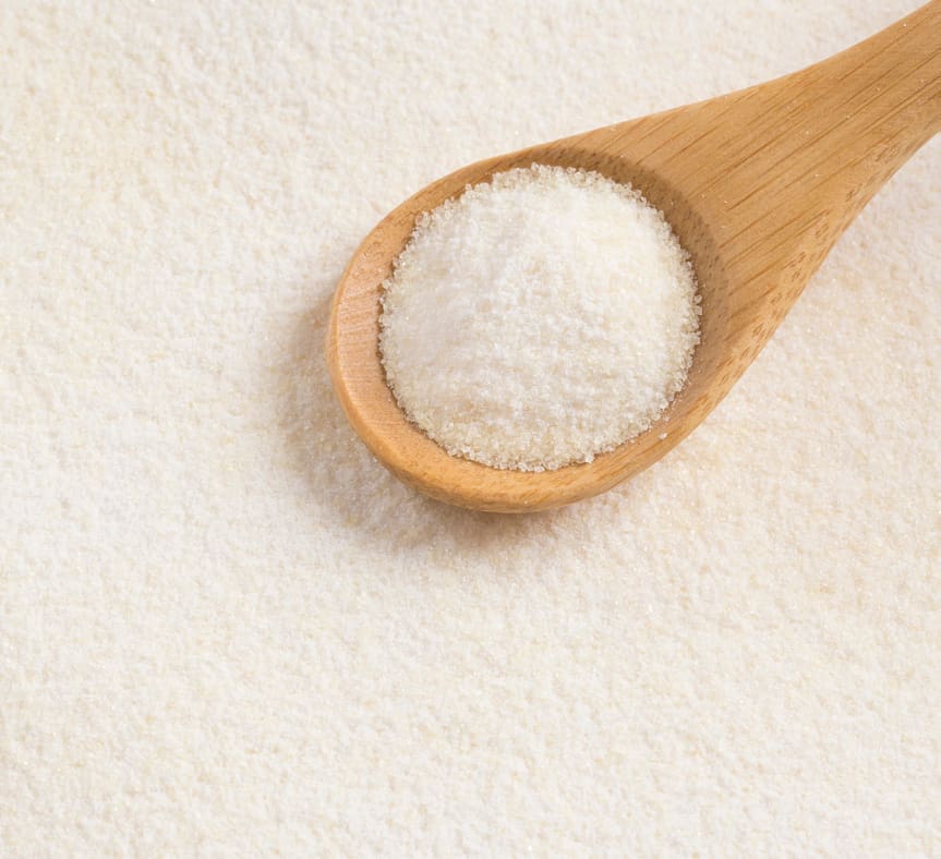 Wooden spoon filled with white collagen powder resting on a surface covered with the same powder.